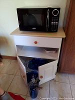 Sunbeam microwave model SGB8901 on top of white wooden cart stand with drawer and cabinet doors, showing front view.