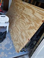 Three sheets of plywood beadboard style panelling stacked against a wall, showing natural wood finish and vertical grooves.