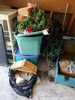 Green plastic tub with artificial Christmas tree decorated with red bows on top, black garbage bag near bottom holds other decorations
