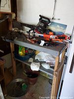 Wooden workbench with various yard tools placed on top and lower shelf, including cordless string edger and blower vac.
