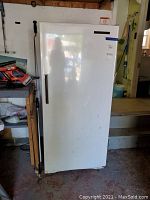 Full front view of the white GE upright freezer in a garage setting showing door with vertical handle and condition of the exterior.
