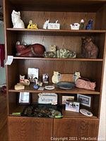 Shelf with about 22 cat figurines and cat decor items in varied materials and colors