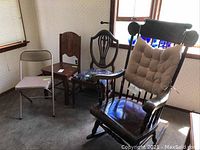 Four chairs side by side in a room showing a metal folding chair, two wooden chairs and a rocking chair.