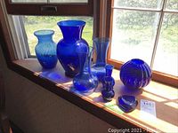 Eight blue glass pieces displayed on a window ledge, showing overall shapes and sizes.