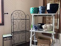 Full view of three items: black metal plant stand, white wooden ladder shelf, and black metal rack with decorative scrolls.