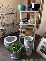 View of the lot including several ceramic planters with varying designs, a white folding stand with planters and a black metal rack.