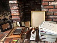 Photo showing collection of eight photo frames of different sizes and materials, six albums stacked boxed, magnifying glass, and two wooden crosses resting by a brick fireplace.
