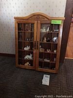 Front view of the wood curio cabinet with two glass doors and visible cat figurines inside.