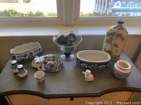 Full view of collection of blue and white ceramic items on counter including pots, cat figurine, pedestal bowl with glass balls, and Bombay salt and pepper shakers