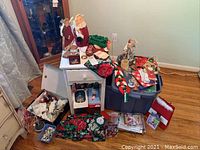 Painted wood accent table with door, open showing holiday paper goods, linens, ornaments placed on and around the table and plastic tote