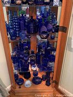 Full view of blue glass collection arranged on three shelves in wooden cabinet with mirrored back