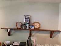 Full view of long wood wall shelf mounted on wall with multiple decorative items including lighthouse figurines, wall clock, framed pictures and other decorative pieces.