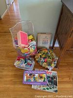 Full view of the lot showing plastic bags with dollhouse furniture, boxed games, and book.