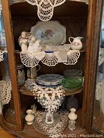 Right cabinet side showing Lladro angel figurines, decorative plates and pitchers, various glass dishes, and doilies