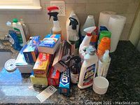 Overview of cleaning bottles, food storage boxes, aluminum pans, and paper towel rolls on kitchen counter.
