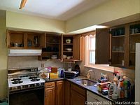 Kitchen corner showing wood cabinets, stove, and countertop with various kitchen items inside the cabinets and on the counter.