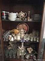 Full view of 3 shelves with various glassware, china pieces, and decorative dishes.