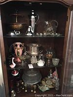 Full view of all items on three shelves inside a wooden cabinet, showing various glassware, barware, and decorative items.