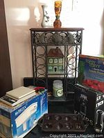 Photo showing ornate metal wine rack with decorative scrollwork, Brita water filter box, small decorative house, candle jar, and cast iron pan with muffin molds.