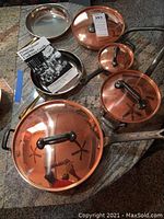 Overview of the copper clad pots and pans including 3 copper lid pots and a frying pan with cast iron handle on granite countertop.