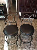 Front view of two metal bar stools with black round cushions showing overall condition.