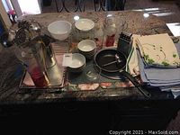 Overview of kitchenware, bowls, glass jars, metal utensils, and folded linens on a countertop.