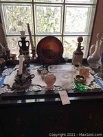 Overview of lot showing candlesticks, glass trinket box, ceramic and glass figurines, and decorative plate on table in natural light