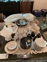 Overview of the lot showing multiple white milk glass serving dishes, Romana cups and saucers, black ceramic cups, various plates, clear glass bowls, and the Capodimonte basket bowl.
