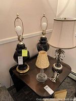 Photo showing all four lamps together on a table: two tall blue lamps without shades, one small lamp with a white shade and crystal base, and one small lamp with a beaded shade and glass base.