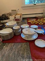 Full view of the collection of plates, bowls, and other china pieces laid out on a table with red cloth.