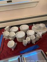 Complete view of plates, cups, and saucers arranged on a red quilted surface, showing the pattern and quantity of items in the set
