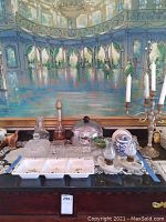 Full lot view showing glassware, metal ice bucket, candlesticks, and assorted ceramic and glass serving pieces on a dark surface in front of a painting.