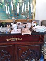 Full view of the lot showing two metal 5-arm candelabras, ceramic bird figurines, stacked plates, ceramic serving dishes, and two sets of flatware with plastic trays.