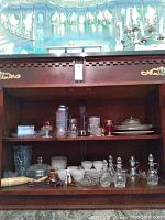 Full view of shelf with assorted glassware, decanters, small dishes, and serving pieces.