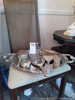 Silver vanity set displayed on a chair including tray, mirror, brushes, perfume bottles, and containers.