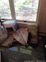 View of multiple linens on floor near window including tablecloths, folded linens, and a small robe in cream and light colors