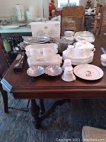 Overview of assorted milk glass cups, dishes, plates, and serving pieces on wooden table