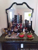 Front view of three blue and gold decorative vases and bowls, two green and red pumpkin bowls, black goblet bowl, black table lamp, and large mirror with black frame behind
