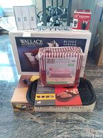 Overall view of all items in the lot including boxed buffet server, furniture protector, wood serving trays, grill pan and car organizer, placed on a granite surface.