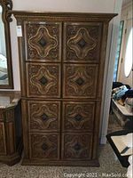Full frontal photo of the vintage armoire showing the detailed carved wood doors with raised molding and metal pull hardware.