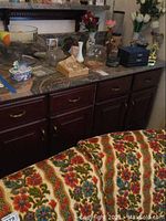 Wide view of the countertop showing all items including glassware, candle, faux flowers, piggy bank, and ashtray.