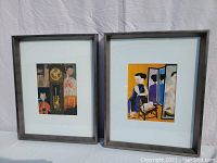 Both prints shown side by side against plain backdrop, featuring women and cats in bright colors within brushed nickel frames
