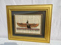 Front view of the framed Winged Isis Egyptian papyrus painting showing gold frame and black/brown mat with hieroglyphics below the figure.