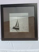 Front view of the large framed and matted black and white photograph of a sailboat on water.