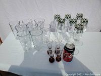 Full set of 19 glasses displayed on table, including 8 clear bubble pattern tumblers, 4 amber bottom shot glasses, 7 decorated champagne flutes, with soda can for scale.