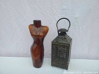 Full lot view showing Italian Murano glass torso vase alongside black metal garden lantern on white draped background.