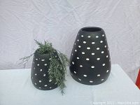 Both planters displayed on a white surface with a plain background. Larger planter is tapered; smaller planter has greenery inside, black with white polka dots.
