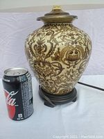 Photo of the ginger jar lamp base with intricate brown floral designs, showing scale next to a soda can.