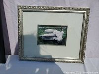 Framed black and white photograph of "The River" statue outdoors, showing photo within white mat and silver decorative frame.