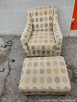 Front view of armchair with polka dot upholstery and ottoman placed in front outdoors on pavement.